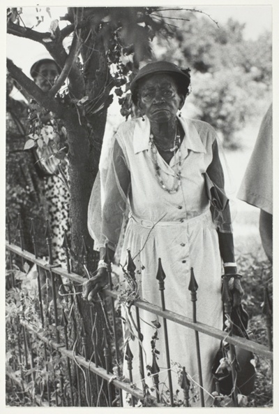 Old Negro Woman Standing by Iron Fence