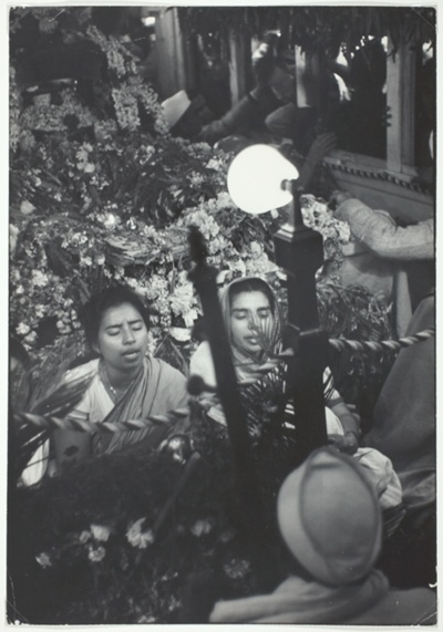 Two Women Sit Reciting Prayers, Facing Light with Mass of Flowers